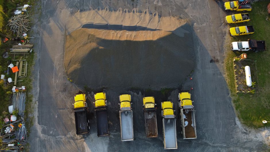 Drone shot of yellow trucks aligned by a gravel heap in New Bern, NC, showcasing industrial work.